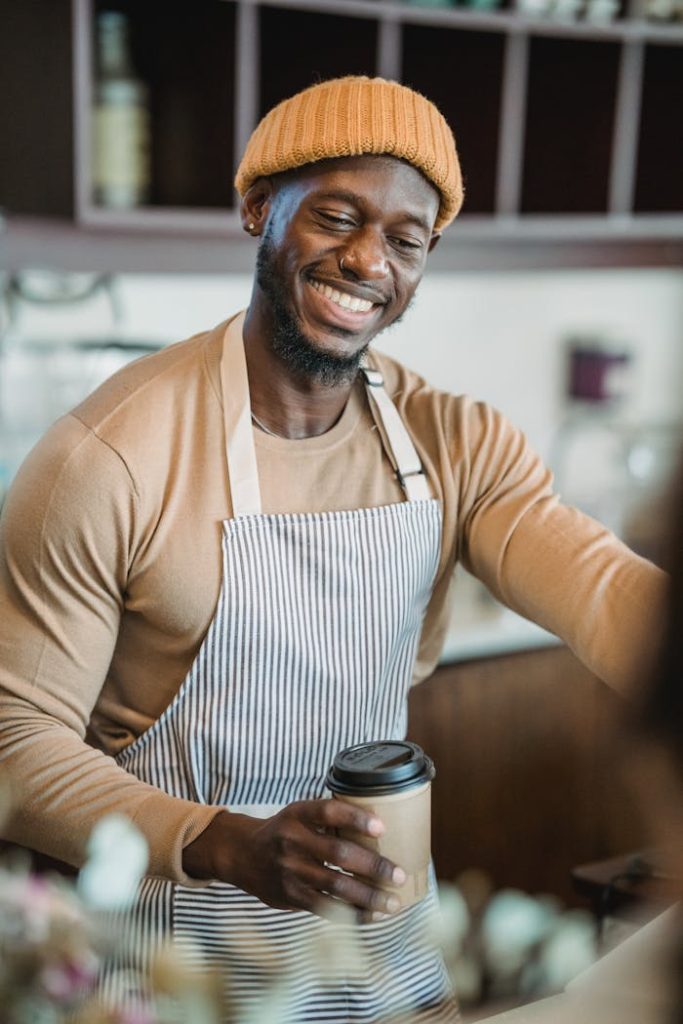 Friendly barista wearing an apron serves a hot coffee with a smile, creating a welcoming atmosphere.